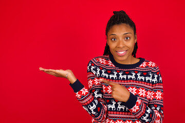 Young beautiful African American woman standing against red background pointing and holding hand showing adverts