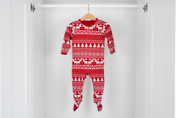 White and red christmas pajamas hanging on a wooden hanger in the middle of a white closet.