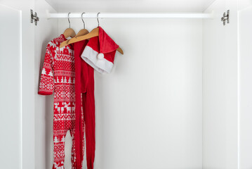 White and red christmas pajamas, hat and tights hanging on a wooden hangers on the left of a white closet.