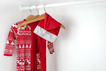 White and red christmas pajamas, hat and tights hanging on a wooden hangers on the left of a white closet.