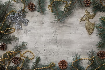 Grey Christmas background with green tree branches, cones and decorations, and with a toy angel, with space for text.