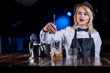 Experienced woman tapster adds ingredients to a cocktail in pub