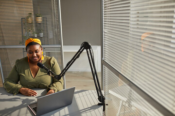 African happy woman sitting at the table and typing on laptop during live broadcast at office