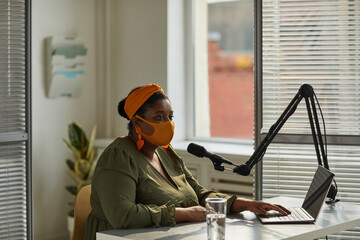 African host in mask speaking on microphone working on radio during pandemic