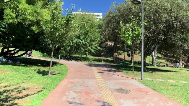 Footage of people walking and relaxing at city park called "Macka Demokrasi Parki" in Istanbul. It is a sunny summer day. Camera moves forward.