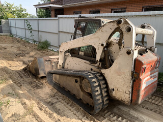 Small tractor with wide bucket. Small construction equipment. The crawler excavator levels the ground.