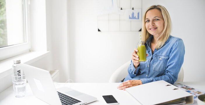 Woman Drinking Green Smoothie In Office