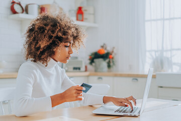 Lady with perfect dark skin holding credit card and inserting bank information for online shopping...
