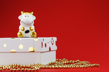 New year's 2021 toy bull with a gift on a red background. Gift box and gold beads.