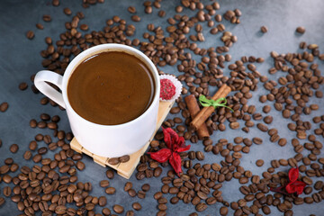 White cup full of coffee beans close up against the dark grey background. Coffee mug. Morning espresso.	