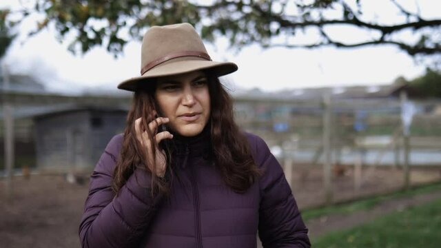 Woman wearing a cowboy hat talking on the phone on a farm