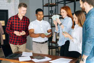 African American man manager giving salary in cash to happy employees after profitable transaction. Cheerful excited young business man and woman throwing away banknote. Concept of money rain.