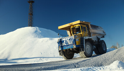 Mining dump truck rushes along the road at the ore-dressing plant against a snow-covered landscape and blue sky, close-up. © esalienko