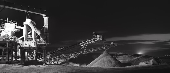 Crusher plant, illuminated by spotlights during operation at night, panorama, black and white. Mining industry.