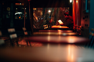 man sitting outdoor alone in a restaurant cafe terrace looking at the menu under a red light