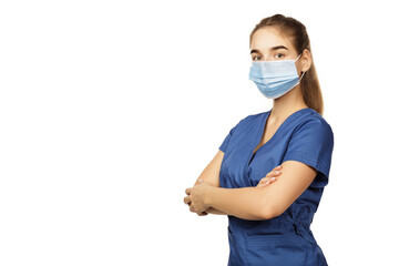 Young beautiful female doctor in blue surgical gown and medical disposable mask on face with folded hands on chest isolated on white