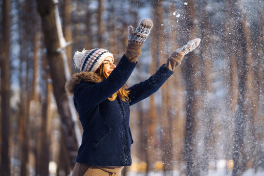Happy winter time. Cute woman playing with snow in snowy forest. Young lady in winter clothes enjoying the winter. Winter holiday. © maxbelchenko