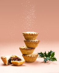 Mince pies stacked on each other on pink background with sugar sifting on top. A mince pie is a traditional Christmas sweet pie, filled with a mixture of dried fruits and spices. - 392238123