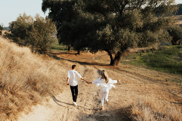 Back of young couple in love is holding hands, running, having fun and enjoying the beautiful nature in the park.