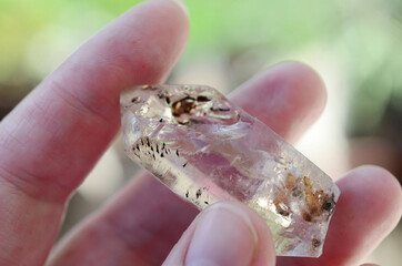Clear quartz being held in woman's hand. Clear quartz point in the sunlight. Healing quartz with inclusions, intricate details. 