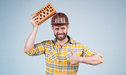 handsome man bricklayer in construction safety helmet and checkered shirt on building site with brick, brickwork