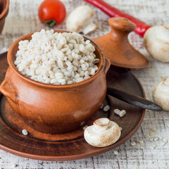 A small earthenware pot with pearl barley porridge on a brown ceramic dish. Russian kitchen. Selective focus.