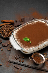 Traditional Italian Tiramisu dessert in glass baking dish and pieces of chocolate bar on concrete...