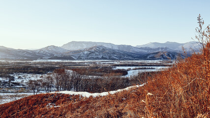 View of snow-covered mountains, river and field from the top of the cliff. Winter landscape in the east of Russia.