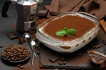 Traditional Italian Tiramisu dessert in glass baking dish, mocha coffee maker and pieces of...