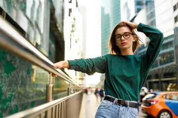 Frontal portrait of a hipster girl with short hairstyle, looking at camera, posing on urban street, at modern buildings background.