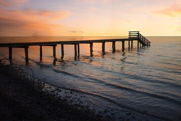 dreamy sunset scenery at stony beach with wooden boardwalk and waves