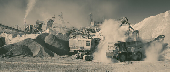 Loading excavator heavy mining truck on the background of stone-crushing equipment at the limestone quarry, monochrome panoramic image imitating an old analog photo printing. Mining industry.