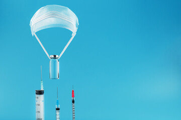 An ampoule with a vaccine against the virus on a shroud of protective grease on a blue background goes down to a row of syringes.