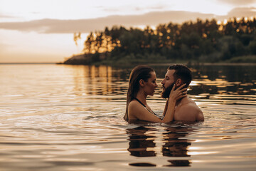 Romantic photo session in the water. A guy and a girl swim in the lake in the evening. Beautiful sunset. © dimadasha
