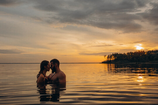 Romantic photo session in the water. A guy and a girl swim in the lake in the evening. Beautiful sunset.