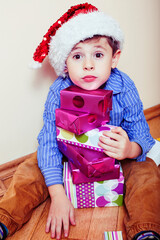 little cute boy with Christmas gifts at home wearing red Santas hat. closeup emotional happy smiling in mess with toys, lifestyle holiday people concept