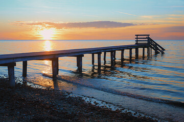 romantic sunset scenery at stony beach with wooden boardwalk and waves