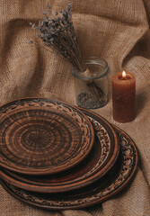 Handmade ceramic craft ware. Rustic napkin and kitchen tools. Plate on a wooden stand with lavender and candle. Handmade ceramic dishes