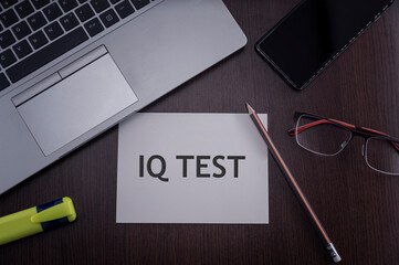 Top view of laptop, phone, glasses and pencil with card with inscription IQ test. Intelligence...