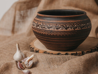 Handmade ceramic craft ware. Rustic napkin and kitchen tools. Jug on a wooden stand with garlic and...