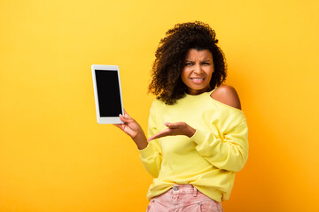skeptical african american woman pointing with hand at digital tablet with blank screen on yellow