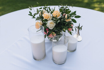 Glass candlesticks with white sand and a bridal bouquet of flowers in a vase stand on a round table like decorations.