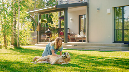 Cute Girl Has fun with Happy Golden Retriever Dog on the Backyard Lawn. She Pets, Play, Tackle it on the Ground And Scratches Back. Happy Dog Plays with Toy Ball. Idyllic Summer House.