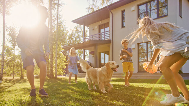 Beautiful Family of Four Play Catch Toy Ball with Happy Golden Retriever Dog on the Backyard Lawn. Idyllic Family Has Fun with Loyal Pedigree Dog Outdoors in Summer House Backyard.