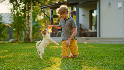 Cute Boy Plays with His Favourite Dog Friend while Having Picnic Outdoors on the Lawn. He Pets and Teases His Little Smooth Fox Terrier with His Favourite Toy. Idyllic Summer House. - Powered by Adobe