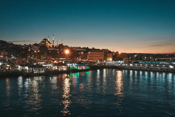 Obraz premium Night view on the restaurants at the end of the Galata bridge, Sultanahmet, at sunset with the famous Suleymaniye Mosque in the background, Istanbul, Turkey,