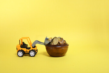 A toy bulldozer lifting coins from a wooden container 