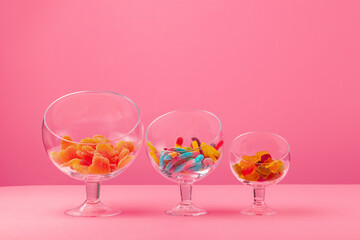Glass containers with candies against pink background