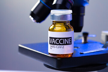 Vial of Covid-19 vaccine next to a microscope