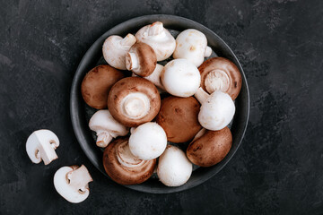 Fresh organic brown and white champignon mushrooms in bowl on dark stone background.